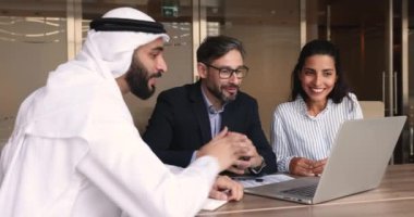 Yatırım konusunda Kandura 'daki Arap mali danışman çift dizüstü bilgisayardaki şirket sunumunu göstererek ofisteki masada oturuyor. Eşlere çevrimiçi emlak sunumu yapan emlakçı