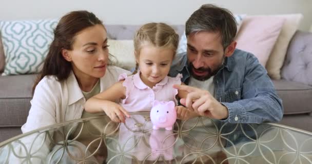 小さな愛らしい娘は 子供に自信を持ってお金を節約することを教える愛する両親 良い金融規則的な習慣 将来のおもちゃや長期的な目標や夢のために保存します — ストック動画