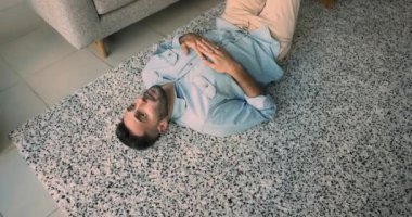 Genç üzgün İspanyol bir adamın rahat bir oturma odasında halının üzerinde uzanması, kendini kararsız hissetmesi, tatsız hayat koşullarını düşünmesi, yalnız görünmesi, tembel görünmesi ya da nedensiz yere evde yalnız zaman geçirmesi.