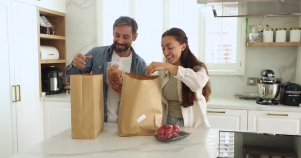 笑顔の若い結婚したカップルは新鮮で自然なプロダクトが付いているペーパー袋を話し 荷を下すこと 共同週末および容易なオンライン スーパーマーケットの食糧配達電子サービスを楽しみます ストック動画
