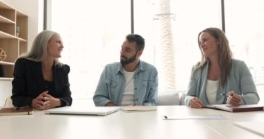 Üç tane etnik çeşitliliğe sahip genç ve olgun meslektaşı konferans odasında konuşuyor, brifing veriyor, stratejilerini paylaşıyor, planlarını paylaşıyor ve modern yönetim kurulunda dostça sohbet ediyorlar. Takım arkadaşları iş akışı