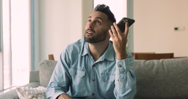 ヒスパニックの男性は 現代のスマートフォンを使用してメッセンジャーを通じて友人と情報を共有し 自宅でソファーに座って 携帯電話を保持し オーディオメッセージを聞き 回答を送信し ボイスメールを記録します テクノロジー コミュニケーション — ストック動画
