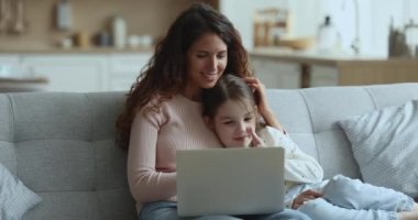 Anne ve küçük çocuk kanepede dizüstü bilgisayarla dinleniyorlar. Sevgi dolu anne, anaokulu kızıyla eğlenmeyi seviyor kanepeye otur, kablosuz bilgisayar ekranına bak, film izle, videoları tartış, internetten alışveriş yap.