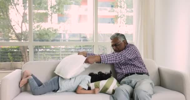 快乐的老曾祖父和小孙子坐在沙发上和垫子打斗 可爱的学龄前男孩抱着枕头玩耍与曾祖父欺骗一起在家里玩乐 家庭游戏时间 — 图库视频影像