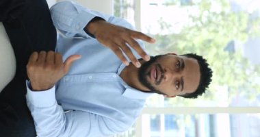 Dikey görünüm yakışıklı Afrikalı adam video çağrısı yoluyla konuşma, kanepeye otur, konuşma yap, kanal için vlog kaydet, haberleri paylaş, arkadaşınla ya da iş ortağınla iletişim kur video konferansı uygulaması kullan