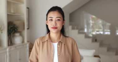 Oturma odasında poz veren gülümseyen Asyalı kadının portresi aşkın sembolü, kameraya bakın, samimi duygularınızı ifade edin, kalp sağlığı için sosyal farkındalık kampanyaları, kişisel bakım, sağlık, gönüllü olma.