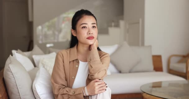 Young Chinese Woman Sits Sofa Home Looking Aside Deep Thoughts — Stock Video