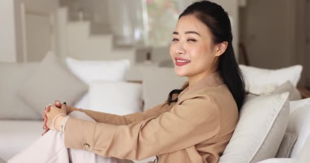 心满意足的中国女人躺在舒适的沙发上 靠在垫子上 看着相机 度过无忧无虑的周末 一个人在家里享乐 陷入愉快的想法和白日梦 — 图库视频影像