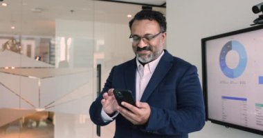 Tatmin olmuş orta yaşlı Hintli işadamı posta kutusunu işaretliyor, cep telefonunda yeni finansal uygulamalar kullanarak satış büyümesi, kar ve gelir hakkında iyi haberler alıyor. İş, finans, ticaret, iletişim