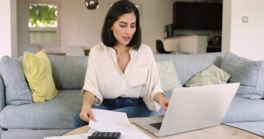 Odaklanmış Latin kadın evdeki kanepede oturur, faturaları e-bankacılık uygulaması ile öder, gelir hesaplar, ev giderlerini kontrol eder, planlar, düzenler. Aile bütçesi, finans yönetimi, tasarruflar