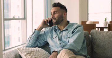 Gülümseyen genç adam koltukta oturur ve cep telefonuyla konuşur, hoş sohbetin tadını çıkarır, kız arkadaşınla sohbet eder, modern teknoloji ve mobil bağlantıları kullanarak hafta sonu tatili planlar. İletişim