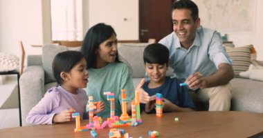 Mutlu Hintli eşler küçük çocuklarla bloklar inşa eder. Kardeşler, sıcak oturma odasındaki masada oturup güzel anne ve babalarıyla oyun oynarlar. Aile hafta sonu tatilleri, oyunlar.