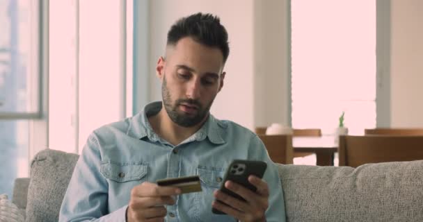 Dissatisfied 30S Man Sit Sofa Hold Credit Card Use Phone — Stock Video