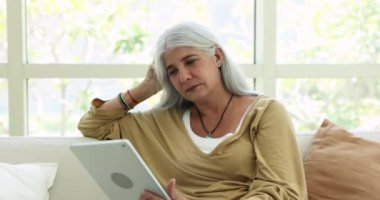 Çekici, orta yaşlı kadın kanepeye uzan, hafta sonunun tadını çıkar dijital tablet kullan. Olgun bir kadın çevrimiçi haberleri okuyor, perakende ekomünikasyon hizmetleri aracılığıyla satın alıyor. Yaşlılar modern teknoloji kullanıyor.