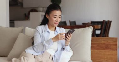 Güzel bir kadın akıllı telefonuyla kanepede dinleniyor, sosyal medyada geziniyor, güncellemeleri öğreniyor, arkadaşlarıyla sohbet ediyor, platformlarda paylaşımlar yapıyor, internette videolar izliyor evde boş vakitlerini internette geçiriyor.