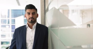 Mutlu Hintli işadamı, başarılı iş sahibi, şık ceketli şirket başkan yardımcısı ofiste yalnız poz veren kameraya bakıyor. Çalışanların portresi yönetici seviyesinde duruyor. Kariyer