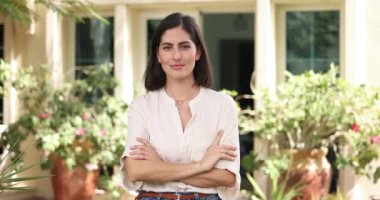 Mutlu Meksikalı kadın kendi arka bahçesinde doğaya poz veriyor ya da kiralık yazlık ev, kollarını kavuşturup gülüyor modern mülkün arka planındaki kameraya bakıyor.