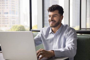 İş yerinde dizüstü bilgisayarda yazan, bilgisayarda çalışan, müşteriyle sohbet eden, başarılı online iletişimin tadını çıkaran mutlu genç Arap serbest iş adamı.