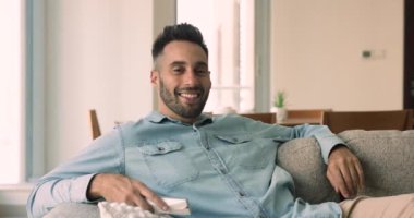 Oturma odasındaki kanepede uzanan neşeli, genç İspanyol adam uzaktan kumandalı komedi filmi ya da futbol maçı izle, televizyon izle, hafta sonları evde TV programının keyfini çıkar.