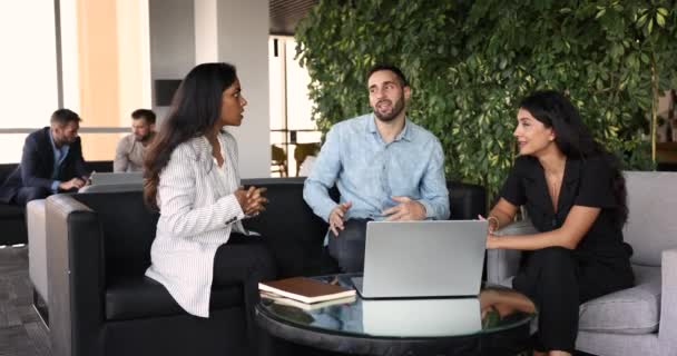 オフィスロビーで会った3人の多民族チームメイトは 居心地の良いワークスペースでノートパソコンとテーブルに座ってアイデアを共有し 問題解決に従事し 戦略を検討し 販売結果とマーケティング計画をレビューします — ストック動画