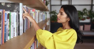 Halk kütüphanesinde kitap seçen güzel bir Hintli kadın. Çekici milenyum iş kadını proje veya kurumsal görev için bilgi topluyor, araştırma edebiyatı, ders kitabı seçiyor, ofiste çalışıyor