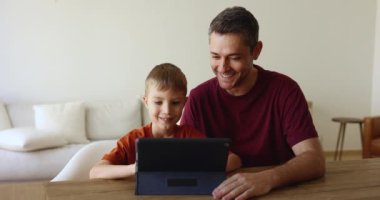 Baba ve küçük 7 'nin oğlu evde oturmuş cihaz ekranına bakıyor, internette eğleniyor yaratıcı hobi için yeni uygulamalar kullanıyor, internetten alıyor, modern dijital tablet kullanarak video oyunu seçiyor.