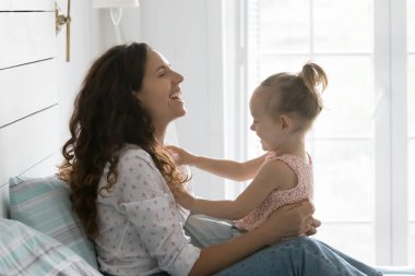 Mutlu gülen anne, anaokulunun sevimli kızıyla sabahları rahat bir yatak odasında vakit geçiriyor. Şirin küçük kız annesinin kucağına oturur ve evde oyun ve iletişimin tadını çıkarır. Aile bağları, annelik.