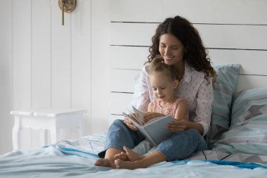Genç ve çekici bir anne, küçük kızıyla yatakta oturur çocuk kitabı okur, ilginç bir masal okur, haftasonunu rahat bir yatak odasında geçirir, boş vakitlerin ve hobilerin tadını çıkarır. İyi yaşam alışkanlığı, gelişme