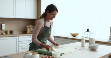 Önlüklü gülümseyen kadın mutfak hamurunu düzleştiriyor, fırın yemekleri hazırlıyor, aile yemeği için tatlı tatlılar hazırlıyor, ev yapımı yemeklerden ve mutfak hobilerinden keyif alıyor. Rutin ve ev işleri