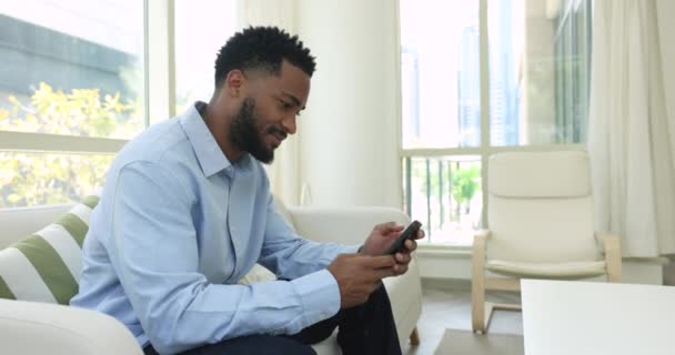 Bonito Camarões Jovem Solteiro Senta Sofá Com Smartphone Usar Aplicativo — Vídeo de Stock