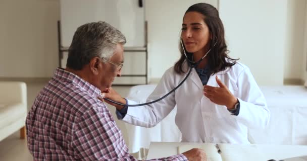 Счастливая Уверенная Молодая Латиноамериканка Осматривающая Старую Индийскую Пациентку Использующая Медицинский — стоковое видео