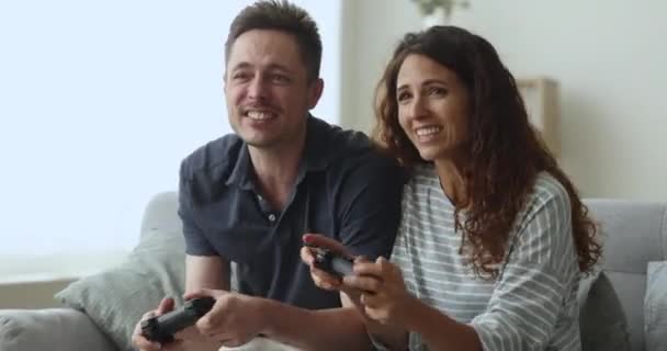 笑顔の妻と夫は家庭で週末を過ごし リビングルームでソファーに座り 仮想世界のチームで電子ステーション戦でビデオゲームをプレイし ハッピーな5を与え 勝利を祝う — ストック動画