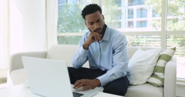Laptop üzerinde çalışan yakışıklı ciddi Afrikalı adam, cihaz ekranına bakar çözüm üzerine düşünür, internette arama yapar, müşteriyle e-posta yoluyla yazışır, cevap üzerine kafa yorar endişeli veya şaşkın hisseder