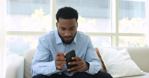 Afrikansk Man Håller Mobiltelefon Prata Med Vän Högtalartelefon Sitter Soffan — Stockvideo