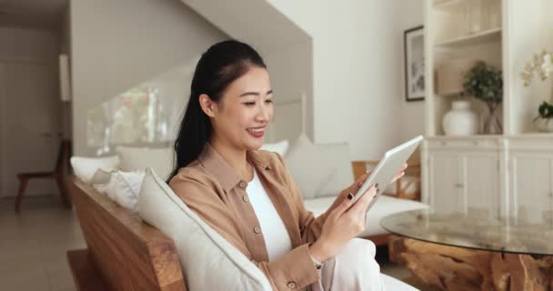アジアの女性は インターネットで自由な時間を過ごし デジタルタブレットでソファーに座り 家族やボーイフレンドとオンラインでチャットし 週末に自宅で電子更新サービスを使用しています ワイヤレステクノロジーの利用 レジャー — ストック動画