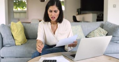 Genç 30 'lu yaşlarda Latin bir kadın evdeki kanepede oturuyor, faturaları ve ücretleri hesaplarken stresli hissediyor, mali zorluklarla, sınırlı gelirle, beklenmedik harcamalarla ve maliyetlerle, kötü mali durumla, borçlarla yüzleşiyor