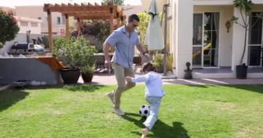 Genç baba ve küçük 8 'lerin oğlu futbola tutkuyla bağlılar, yeşil çimlerde koşuyorlar, top oynuyorlar, güneşli bir yaz gününde kır evinin arka bahçesinde futbol oynuyorlar. Aktif hafta sonu, hobi