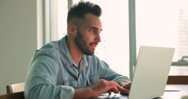 英俊的西班牙男人坐在办公桌前 带着笔记本电脑 浏览网页 浏览互联网 搜索有用的信息 在互联网上花时间 在办公室里滚动社交媒体工作 远程工作 现代技术 — 图库视频影像