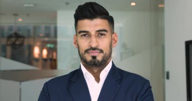 Modern ofis çalışma alanında tek başına kameraya poz veren zarif ceketli, gülümseyen Hintli işadamı. İş başarıları, antrenör ya da şirket patronu portresi