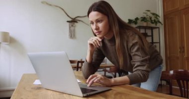 Düşünceli bağımsız iş kadını laptopta yazan, yüzünü çeviren, çeneye dokunan, iş üstünde düşünen, internet projesinde çalışan, masaya yaslanan.