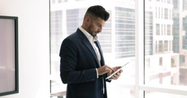 Finansal danışman veya analist, modern gökdelen ofisinde ayakta duran, dijital tableti tutan, mali raporu inceleyen, pazar eğilimlerini analiz eden, müşteriler veya meslektaşlarla iletişim kuran,