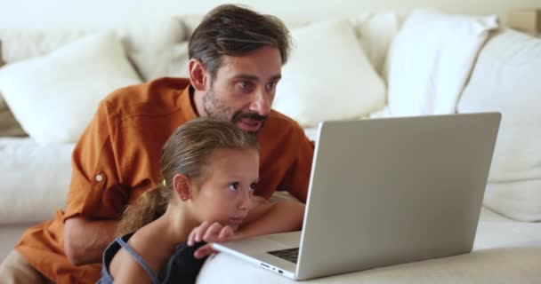 快乐的爸爸和女儿在笔记本电脑上看家庭在线电影 在舒适的客厅里休息 欣赏有趣的卡通片 在网上度过无忧无虑的周末 选择商品 在家里的娱乐时间上网购物 — 图库视频影像