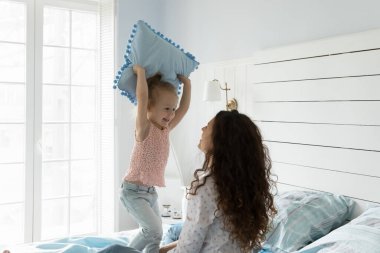 Neşeli küçük bir kız, yatak odasında genç bir anneyle, yastıklı bir kızla, annesiyle oynayarak, sabahları evde kavga ederek eğleniyor. Mutlu aktif aile eğlenceleri, çocuklarla oyunlar, kravatlar.