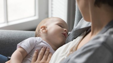Sevgi dolu bir anne kucağında uyuyan şirin bir bebek, yeni doğmuş bebeği sakinleştiriyor, sevgiyle çocuğa bakıyor, şefkat anının tadını çıkarıyor, evdeki koltukta rahatlıyor. Bebeklik, mutlu annelik