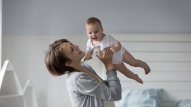 Genç 25 'li yaşlarda çekici bir anne, uyanmış bir bebek bezi ve rahat bir yatak odasında bebek bezi ile oynar, neonata etmek için koşulsuz sevgisini gösterir, mutlu anneliğin tadını çıkarır ve evde paha biçilemez bir zaman geçirir.
