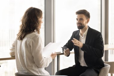 Proje raporlarını, yasal belgeleri, işbirliğini, ortaklığı, çalışma masasında konuşmayı, büyük ofis penceresinde buluşmayı tartışan genç ve olumlu iş arkadaşları.