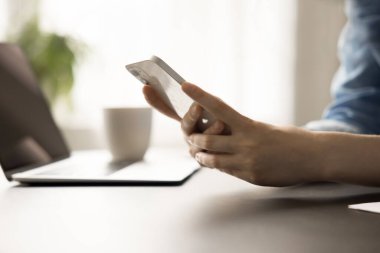Beyaz cep telefonu, iş yerindeki kadınların elinde dizüstü bilgisayarı ve bulanık arka planı olan bir masa. Genç iş kadını, ofis çalışanı, çalışan kadın iş iletişimi için akıllı telefon kullanıyor.