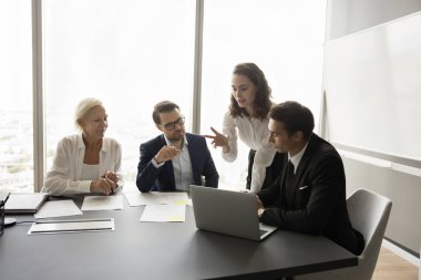 Proje üzerinde birlikte çalışan profesyonel meslektaşlar, dizüstü bilgisayardan proje içeriğini izliyorlar. Genç yönetici, konuşmacı kadın iş planı sunuyor, takıma bilgisayar stratejisi