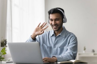 Neşeli genç proje yöneticisi evden video görüşmesiyle konuşuyor, iş için internet iletişimi için dizüstü bilgisayar kullanıyor. İnternetteki konferansta konuşan kulaklıklı genç Hintli.