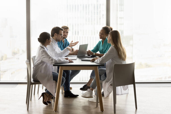 Разнообразная команда больничных врачей, встречающаяся за столом, говорящая о сотрудничестве, командная работа в больнице, обсуждающая сложные случаи заболевания, слушающая говорящего медицинского эксперта. Широкий выстрел